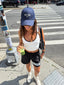 Stride Crop in White, street-style photo of model on a New York crosswalk wearing the white crop with black shorts and a navy cap, holding a green juice