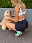 Stride Sports Bra in White and Stride Shorts in Black, back view of model crouching on a footpath to pat a fluffy dog