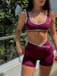 Stride Shorts in Crimson, lifestyle photo of model on a sunny balcony, styled with a matching Stride Sports Bra, showing white piping and criss-cross waistband