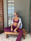 Stride Flares in Crimson, lifestyle photo of model in sunglasses seated cross-legged on a timber bench, styled with a matching Stride Sports Bra and a light blue shirt over her shoulders