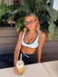 Stride Sports Bra in White, lifestyle photo of model in sunglasses seated at a café table with an iced coffee, wearing the white sports bra with black piping