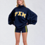 A woman modeling an oversized navy blue sweatshirt with 'PXM' in yellow varsity lettering across the chest, paired with matching navy athletic shorts featuring yellow side stripes, against a light gray studio background.
